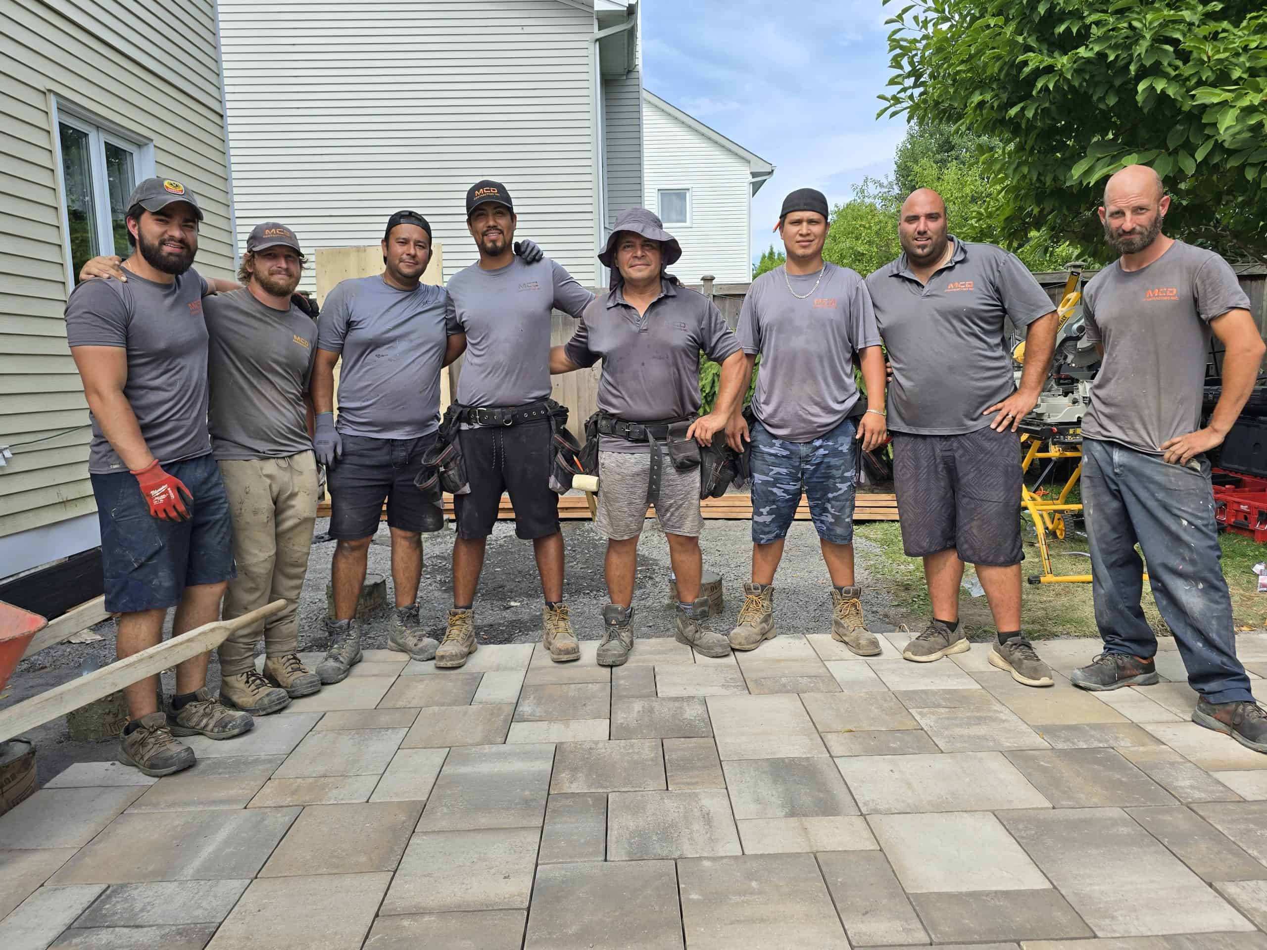 MCD Contracting Inc. jobsite crew of eight men standing together on a new paver patio, demonstrating their capacity