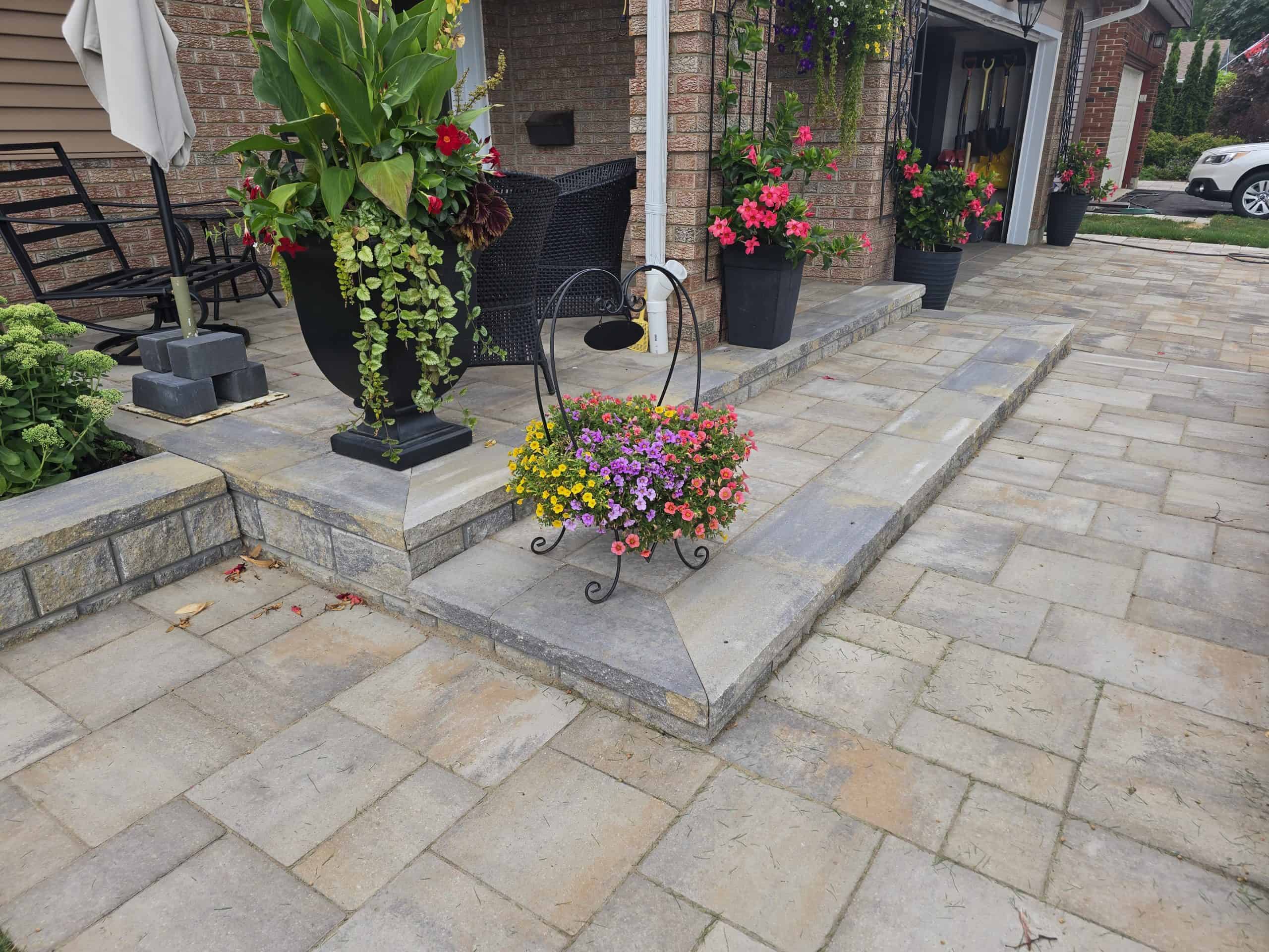 This beautiful interlock patio and walkway showcases expert craftsmanship, featuring a raised landing with a ramp and vibrant floral arrangements.