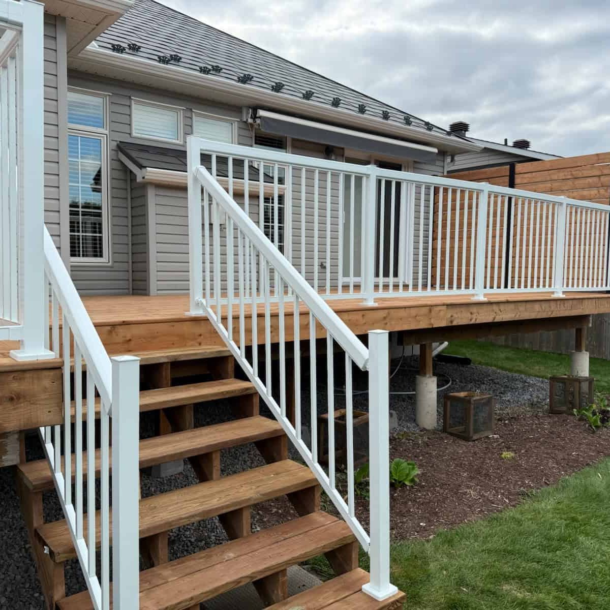 Deck white railing stairs yard shows a new elevated wooden deck with safe white railings and steps, transitioning cleanly to the backyard lawn.