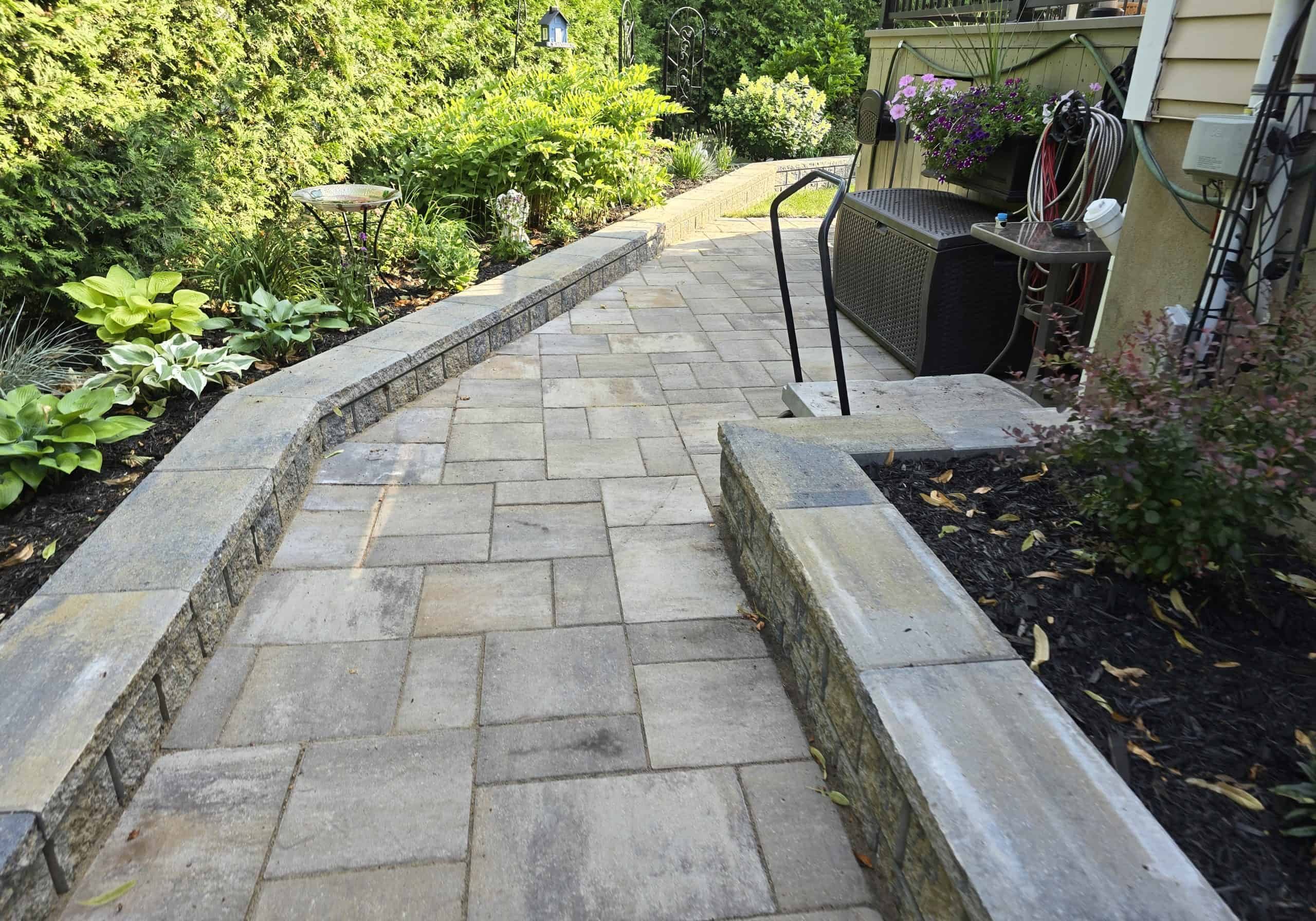 Inviting paver walkway bordered by low retaining walls, seamlessly connecting the home to the lush backyard garden with easy, accessible steps.