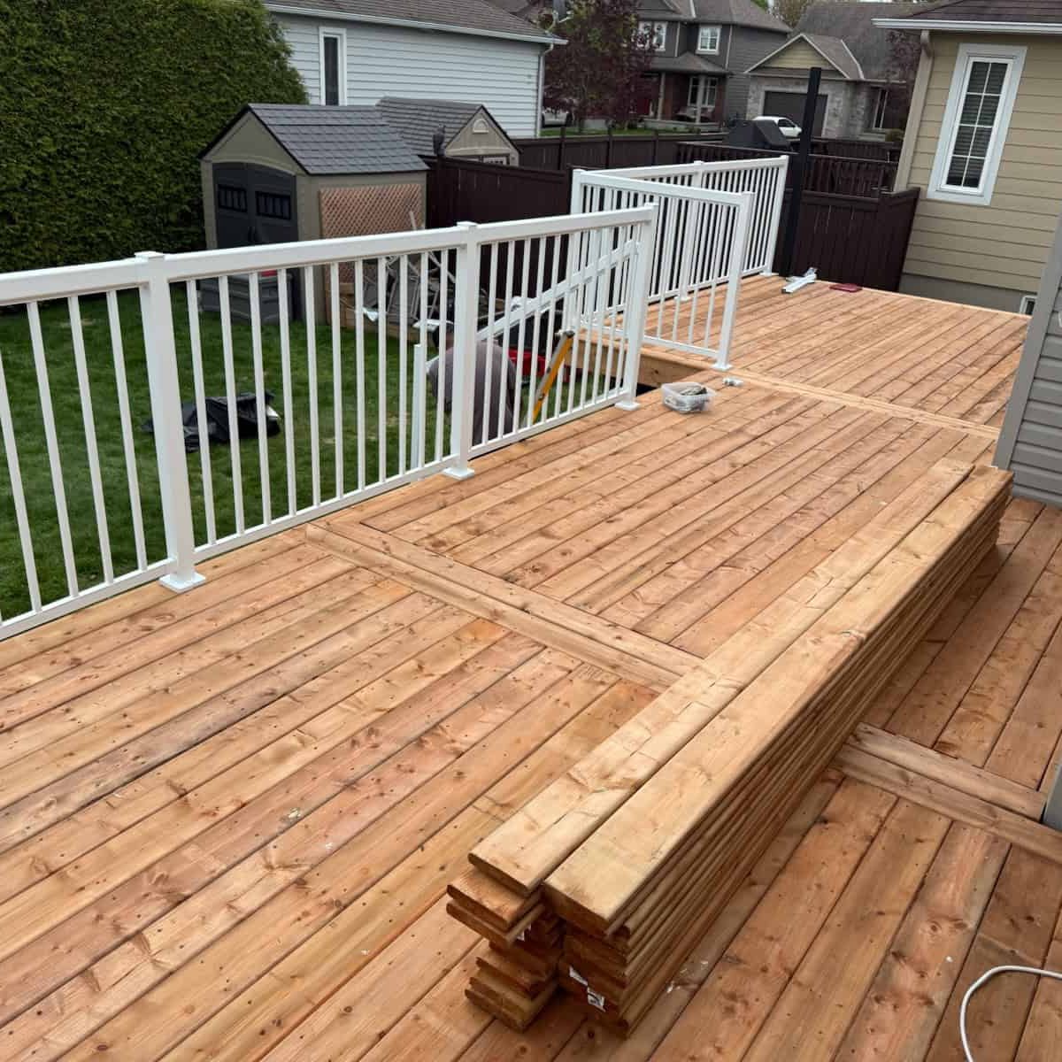 New wood deck and white railing under construction. The large, custom-patterned deck uses warm-toned wood, complemented by clean white railings.