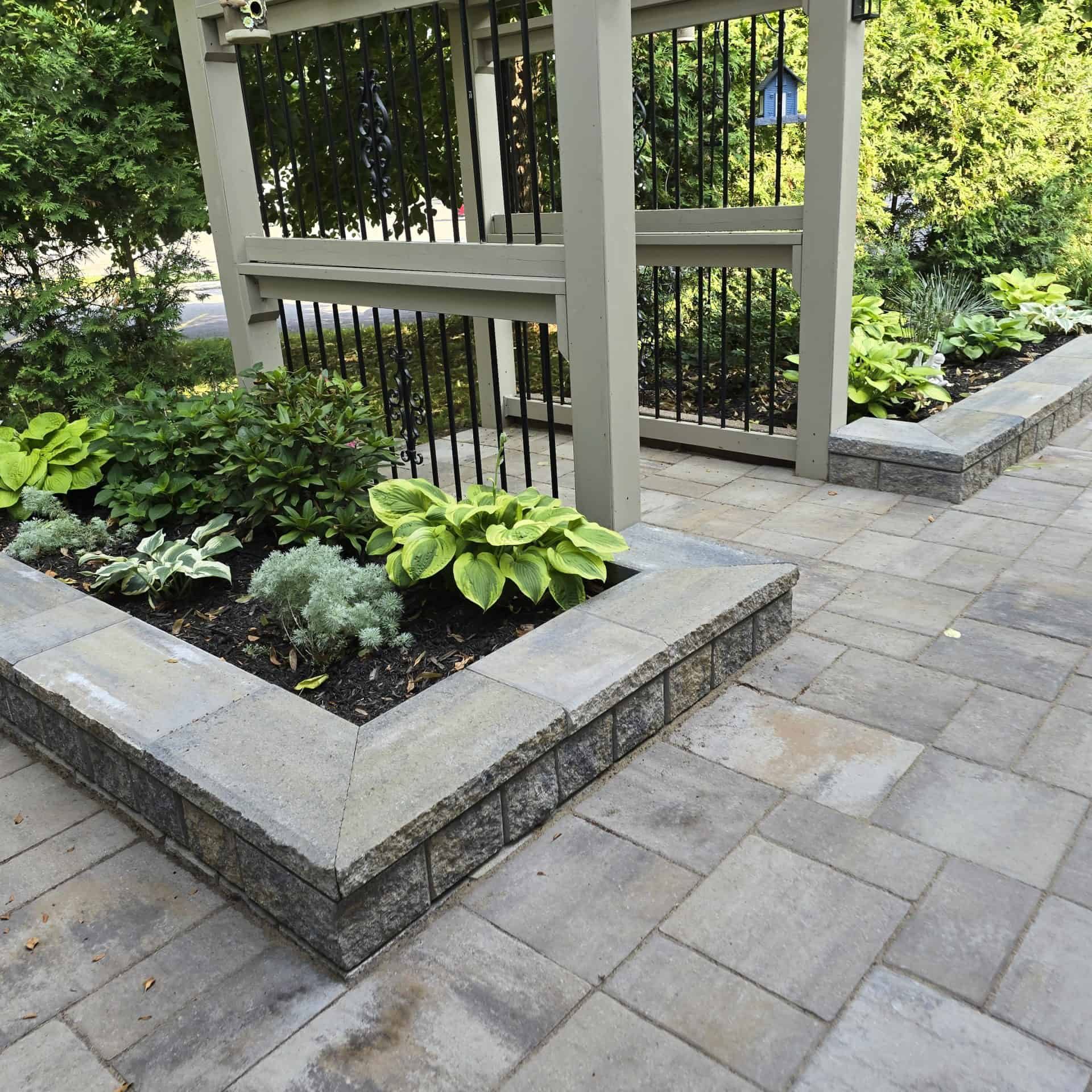 Custom paver patio leading to a beautiful raised garden bed and pergola. Expert hardscaping that creates a functional, lush outdoor living space.