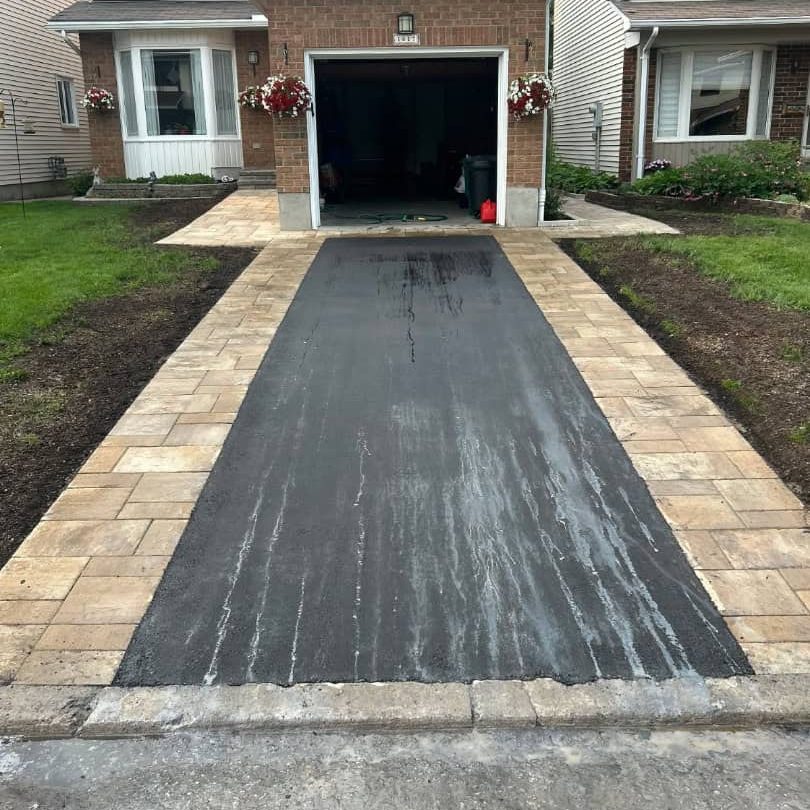asphalt page Driveway paver border asphalt installation. The tan interlocking pavers provide a premium, durable edge framing the new black asphalt surface.